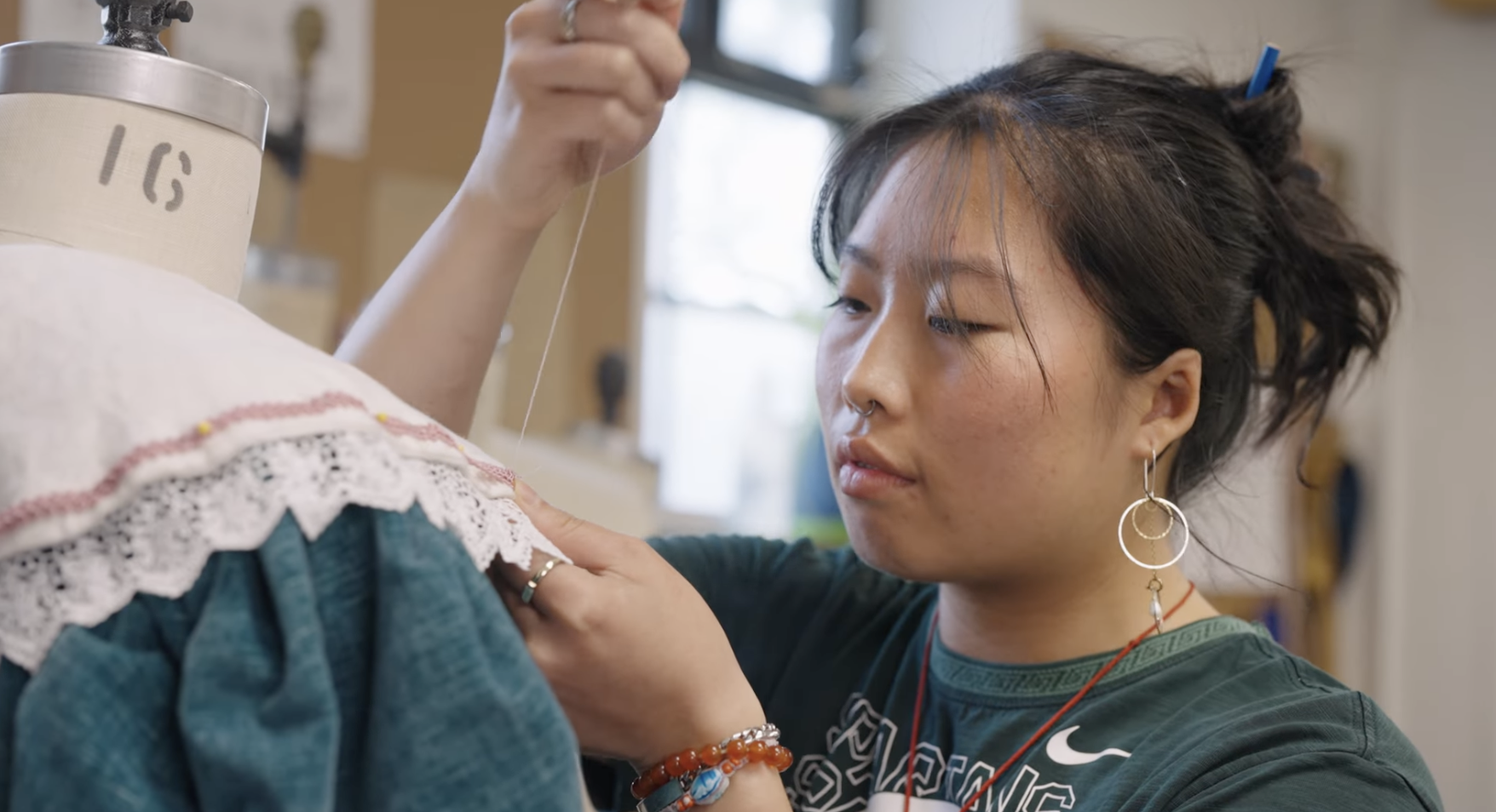 Student Kathrin Poon sews a ruffled color onto a green dress